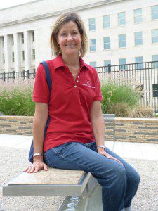 Laurie Laychak seated on the bench dedicated to her husband David Laychak, who was killed in the 9/11 attack on the Pentagon’s southwest wall (pictured behind her).